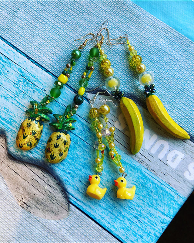 This picture is of 3 sets of dangle earrings; the pairs from right to left feature a pineapple, a yellow rubber duck and a banana as the drop, all created by Carol Triocchi.